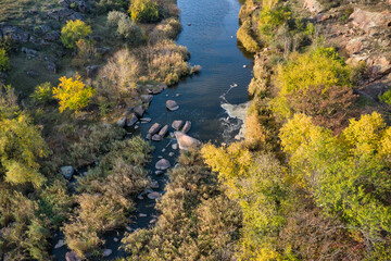 A picturesque stream flows in the Aktovsky Canyon, surrounded by autumn trees and large stone boulders