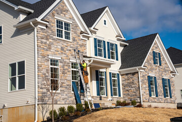 Double gable with colored stone facade siding, with white frame, vinyl shutters © Victor