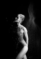 A high contrast photo of a ballet dancer girl wearing a bodysuit with flour flying around her body on a black background. Artistic, commercial, monochrome design