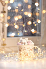 Marshmallow in a Christmas Cup. The Cup stands on a window decorated with a garland.