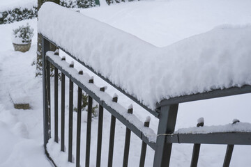 snow covered black metal handrail by the house across snowy backyard. Winter season