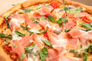 Pizza with prosciutto, cherry, arugula and basil in a cardboard box
