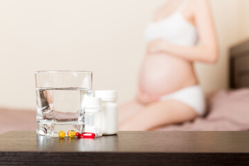 Attractive sick pregnant woman is lying in sofa. Taking pills from colds