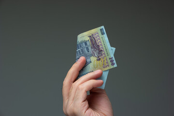 Caucasian male hand holding a folded 100 Romanian lei bill close up shot isolated on gray