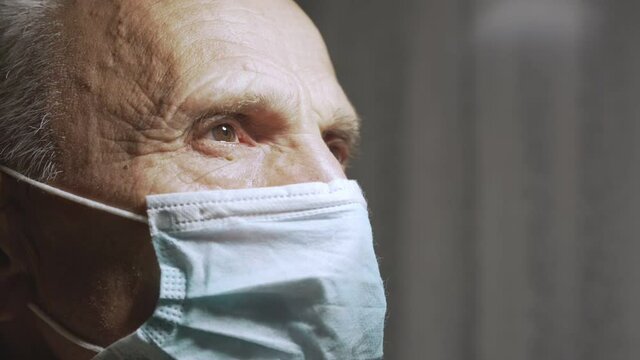Side view of face of senior man wearing protective facemask and opening and closing eyes