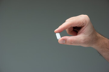 Caucasian male hand holding a white medicine pill between fingers close up shot isolated studio shot