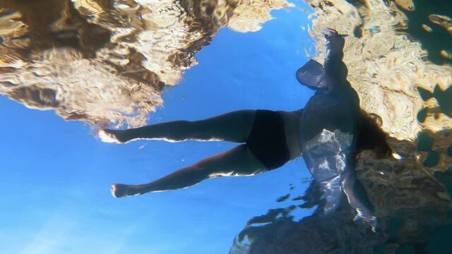 Girl swims and relaxes in sea during vacation, underwater shooting from below with action camera. Dead body of drowned woman floats on surface of water