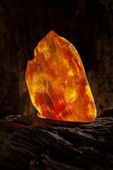 Beauty of natural raw amber. A piece of yellow opaque natural amber on large piece of dark stoned wood.