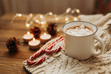 Delicious hot drink chocolate or cocoa with marshmallows Christmas canes candy candles lights and garlands in the background. Winter time. Christmas and new year concept