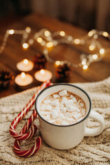 Delicious hot drink chocolate or cocoa with marshmallows Christmas canes candy candles lights and garlands in the background. Winter time. Christmas and new year concept
