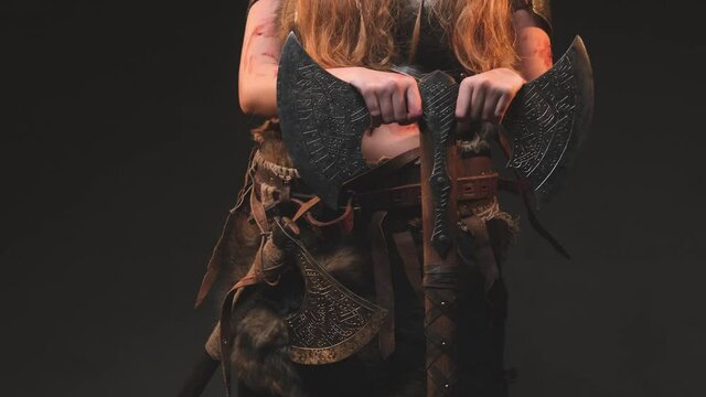 Body of northern and barbaric female warrior dressed in ragged clothing with antique steel armour holding a two handed axe in dark background. Portrait of a scandinavian valkyrie.