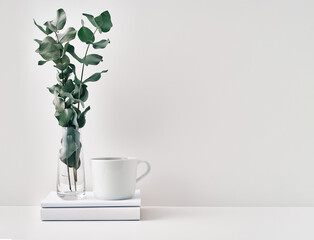 A mug, a stack of books, a wooden board and a transparent vase with eucalyptus branches. Eco-friendly materials in interior decor, minimalism. Copy space, mock up