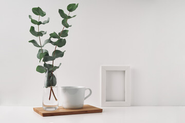 Frame, vase with eucalyptus and a cup on a wooden board, white background. Mock up, copy space. Folk.