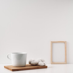 Frame, cotton and a cup on a wooden board, white background. Mock up, copy space. Folk.