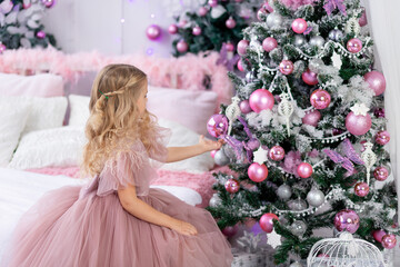baby girl dresses up the Christmas tree in a beautiful pink dress, new year and Christmas concept