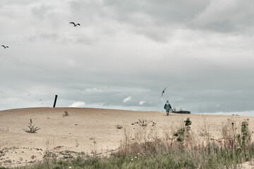 Cloudy sky and sand, in the background a man in a green raincoat. Travel in any weather.