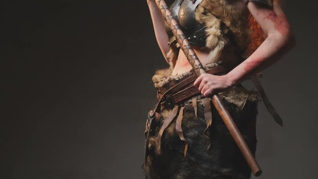 Body of northern and barbaric female warrior dressed in ragged clothing with antique steel armour holding a two handed axe in dark background. Portrait of a scandinavian valkyrie.