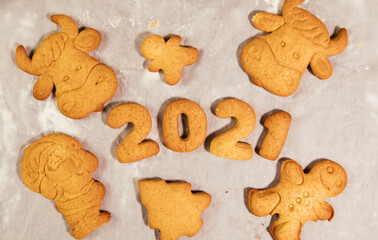 Woman hand cutting cookies, year 2021 on dark board with baking flour. rolling pin, flour and shape of new year figures.