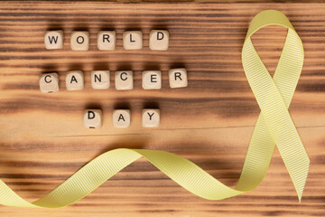 Wooden cubes with World Cancer Day text and yellow ribbon on a wooden surface. Flat lay