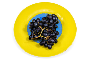 A bunch of ripe black grapes on yellow plate on white background, isolated.