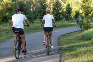 Fototapeta premium A man and a woman riding their bicycles in a park in summer in the sunny morning.