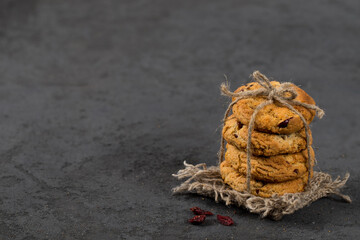 Oatmeal cookies with dried cranberries, tied with jute thread on a linen napkin on a dark gray background in rustic style copy sapce