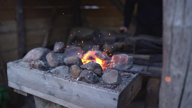 Fire crackling in blacksmith workshop of forging metal. Anonymouse craft smith create objects from wrought iron or steel with helper. Slow motion 4K footage.