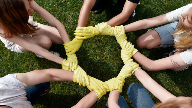 Collaboration. Group of young people, volunteers wearing protective rubber gloves putting their hands together while cleaning up a park