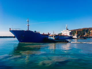 The tugs work in tandem to turn the ship out of the harbor on a sunny day.