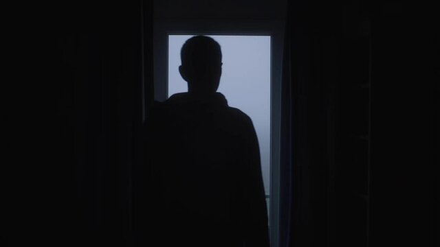 Man stands in front of a window, then he closes the curtain.