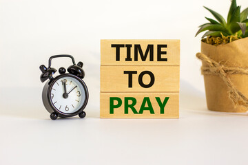Time to pray symbol. Wooden blocks with words 'time to pray'. White table. Black alarm clock and house plant. Beautiful white background. Copy space. Religion and time to pray concept.