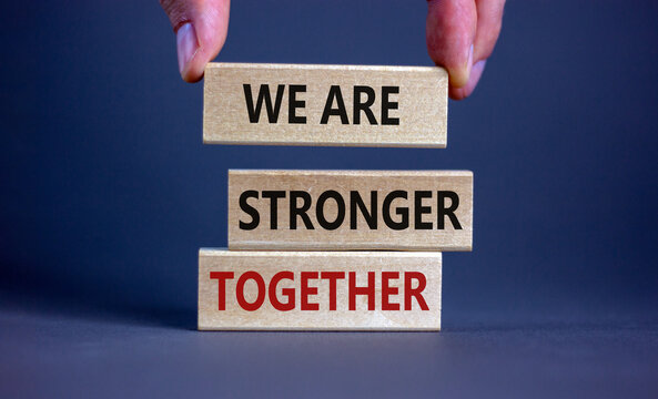We are stronger together symbol. Wooden blocks form the words 'we are stronger together' on grey background. Male hand. Business and we are stronger together concept. Copy space.