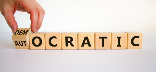 Democratic or autocratic symbol. Male hand turns a cube and changes the word 'autocratic' to 'democratic'. Beautiful white background, copy space. Business and democratic or autocratic concept.