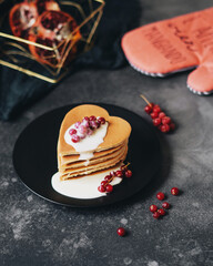 Breakfast for lovers. The heart-shaped pancakes are topped with sweet cream and decorated with fresh red currants. Ideas for Valentine's Day. Fresh pomegranate in the background. Nice food.