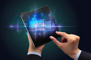 Businessman holding a foldable smartphone with VIRTUAL inscription, new technology concept