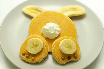 Creative meal for a child, pancake with banana, chocolate and whipped cream in a rabbit shape