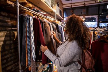 African American black woman with curly hair is shopping for clothing at a local shop. she is browsing through many pretty items to purchase at a good discount