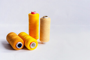 Four different shades of yellow colored sewing thread spools on isolated white background.