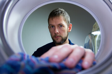 Young caucasian man take clothing out from washing machine. Man making houseworks