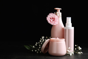 Set of hair cosmetic products and flowers on stone table against black background. Space for text