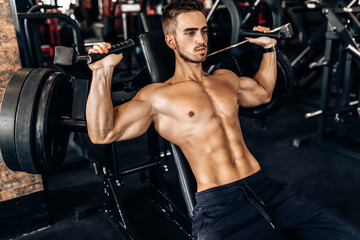 Fototapeta na wymiar young muscular man, shirtless, working out in the gym, doing chest and arm exercises
