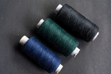 Fototapeta na wymiar Black, deep green and deep blue colored sewing thread spools on isolated black background.