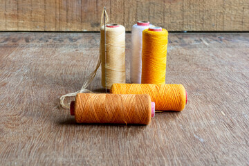 Three different shades of yellow, brown and a white colored sewing thread spools with needle on...