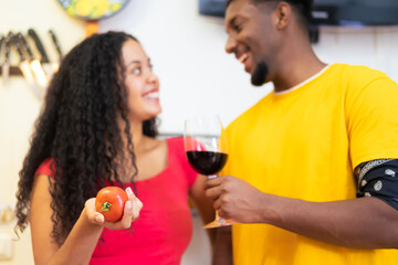 Romantic couple at home. Attractive young woman and handsome man are enjoying spending time together while standing on traditional kitchen. Love and food concept. Focus on tomate.