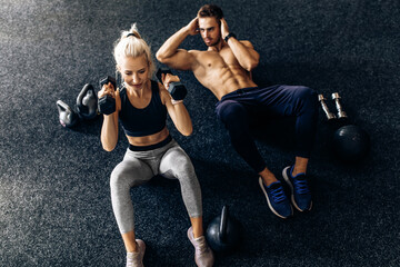young couple, man and woman doing abdominal exercises with dumbbells, on the floor in the gym
