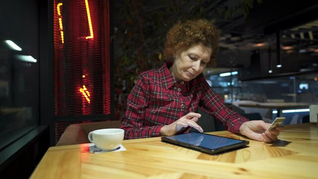 Senior woman ordering Christmas gifts online on digital tablet in coffee shop. Mature buyer holding tablet pc and credit card. Elderly woman shopping online. Online personal finance. Black Friday