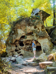 A girl looks up at a rock with many holes on a summer day in the forest