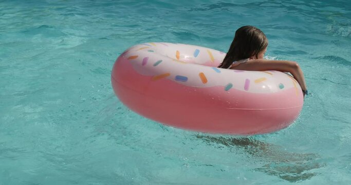 beautiful young girl playing with her inflatable donnuts in the swimming pool