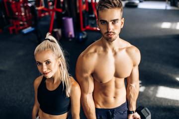 Fototapeta na wymiar Sporty couple, muscular man and woman, in sportswear, train with dumbbells in the gym