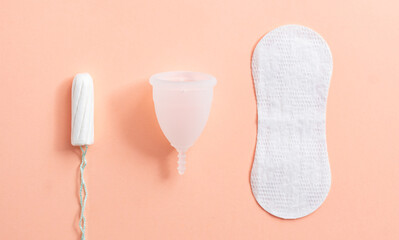 Menstrual hygiene products including tampon, menstrual cup and sanitary pad on peach background